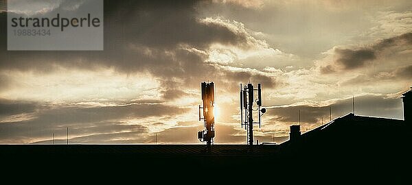 Silhouette eines Fernmelde oder Mobilfunkmastes auf dem Dach eines Gebäudes  Abendsonne