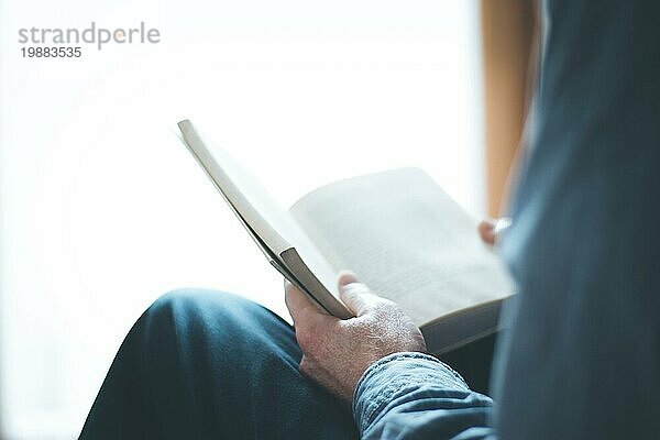 Ausgeschnittenes Bild eines älteren Mannes  der zu Hause ein Buch liest