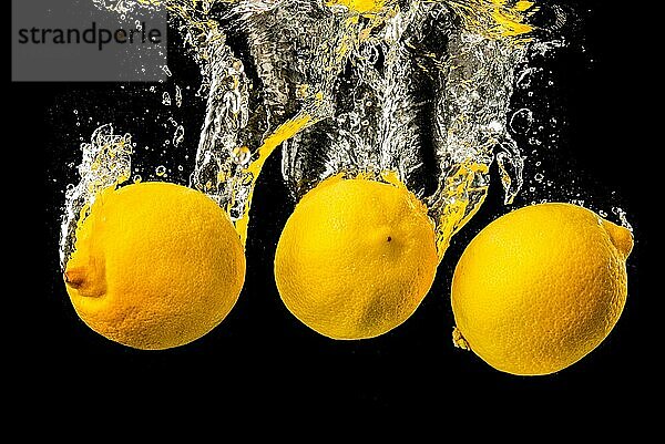 Frische gelbe Zitronen in Wasser spritzen auf schwarzem Hintergrund mit vielen Luftblasen. Erfrischung Konzept