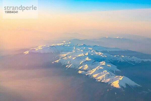 Luftaufnahme von bunten Sonnenaufgang über Berge Schneespitzen und Silhouetten  aus dem Flugzeug geschossen