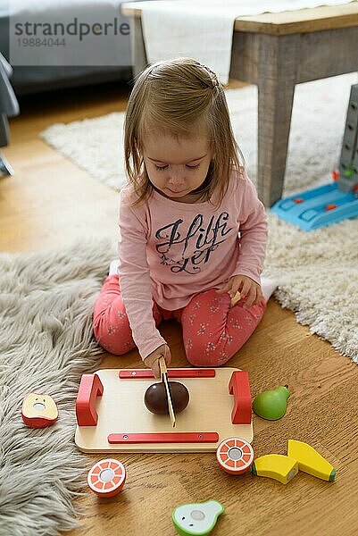 2 Jahre altes Baby Mädchen zu Hause Schneiden woden Spielzeug Früchte mit Holzmesser. Kind Entwicklung Konzept