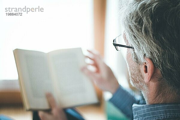 Ausgeschnittenes Bild eines älteren Mannes  der zu Hause ein Buch liest