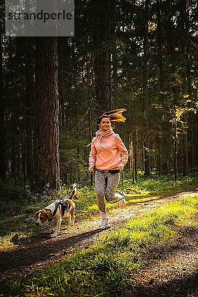 Junge Frau und Hund laufen zusammen auf dem Land im Wald. Fröhliche Frau  die mit ihrem Haustier im Freien trainiert. Aktive Menschen Konzept