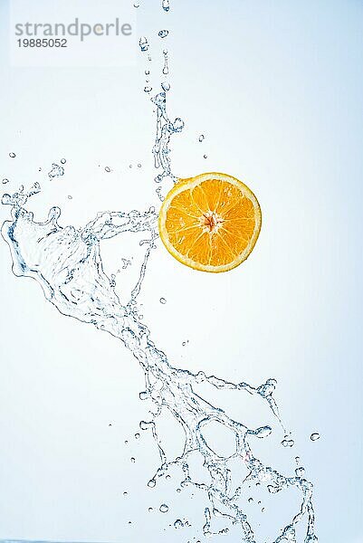 Eine halbe Orangenfrucht mit Wasserspritzern in der Luft  vorhellblauem Hintergrund. Erfrischung Konzept