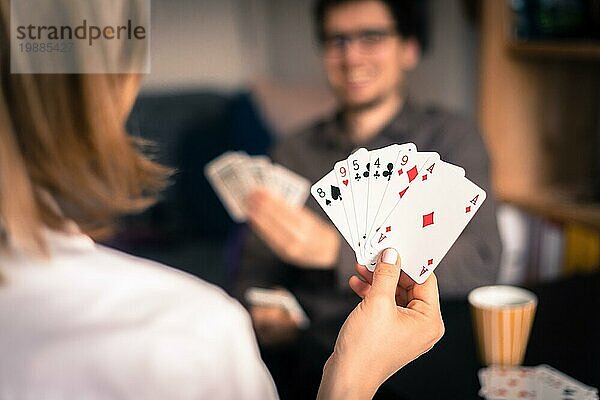 Kartenspielen zu Hause: Freunde sitzen an einem Tisch. Frau spielt Karten  Mann im unscharfen Hintergrund