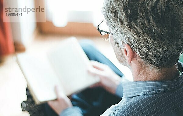 Ausgeschnittenes Bild eines älteren Mannes  der zu Hause ein Buch liest