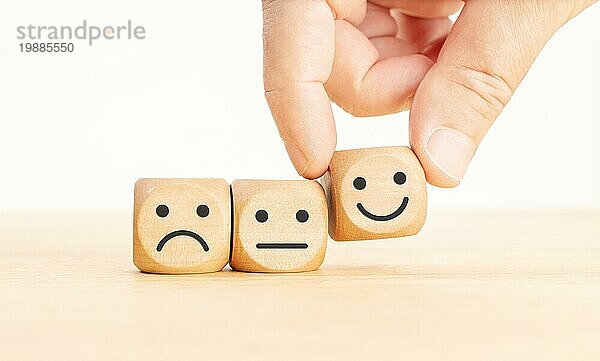 Konzept zur Bewertung des Kundendienstes. Hand Kommissionierung der glücklichen Gesicht Emoticon auf Holzblock
