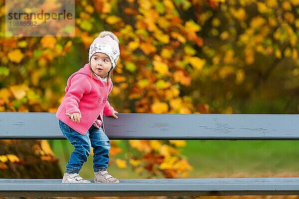 Baby Mädchen im Herbst Park auf einer Bank stehen. Herbstmotiv im Hintergrund. Eggenberg Park in Graz Österreich