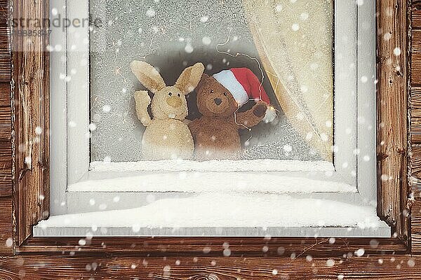 Zwei niedliche Spielzeugfreunde begrüßen den verschneiten Weihnachtsabend und beobachten den Schneefall durch das gefrorene Fenster