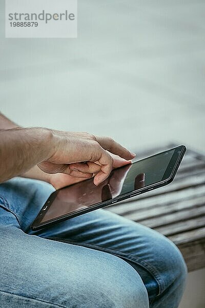 Ein Student sitzt im Freien auf dem städtischen Campus und arbeitet mit einem Tablet PC. Nahaufnahme