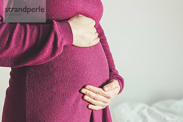 Nahaufnahme eines schwangeren Bauches  kaukasische Mutter im magentafarbenen Kleid