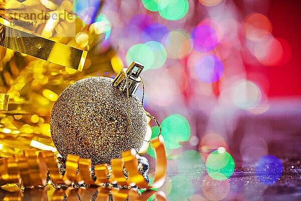 Goldfarbene Weihnachtskugel mit Lametta und Band auf Spiegelfläche und unscharfem Hintergrund
