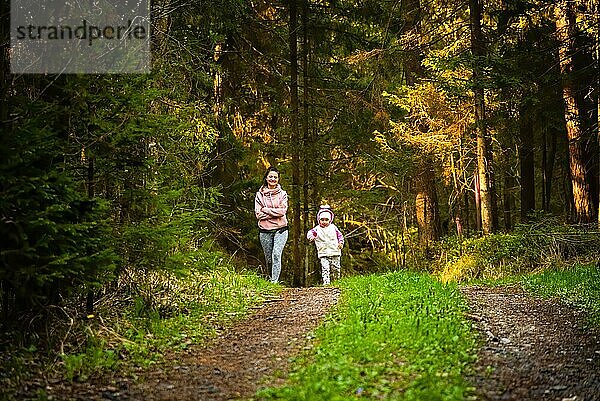 Junge Frau mit 2 Jahre alten Tochter zusammen läuft auf dem Land im Wald. Fröhliche Frau trainiert mit ihrem Kind im Freien. Aktive Menschen Konzept