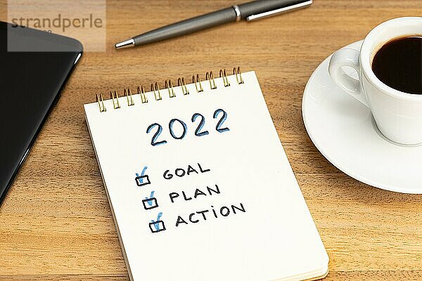 Neues Jahr 2022 Ziel  Plan  Aktion Text auf Notizblock und Kaffeetasse und Smartphone auf Holztisch. Business Motivation Konzept