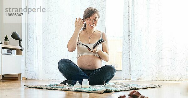 Glückliche kaukasische schwangere Mutter sitzt auf dem Boden und liest über Schwangerschaft  Blue Jeans