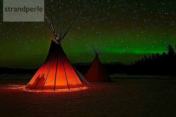 Zwei Zelte  Tipis  Indianerzelte  vorderes von innen beleuchtet  in Winterlandschaft  am Himmel Polarlichter (Aurora borealis) mit Sternen  Yukon Territory  Kanada  Nordamerika