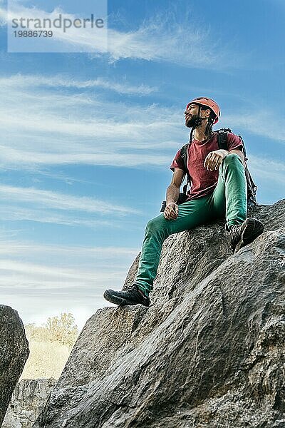 Junger Mann mit Sicherheitshelm und Kletterausrüstung  der sich auf dem Gipfel eines Berges ausruht