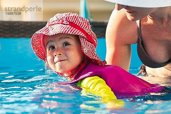 23 Jahre altes Kind mit Mutter im Schwimmbad lernen zu schwimmen. Baby im Schwimmen Westen und roten Hut.Sommer zu Hause Konzept