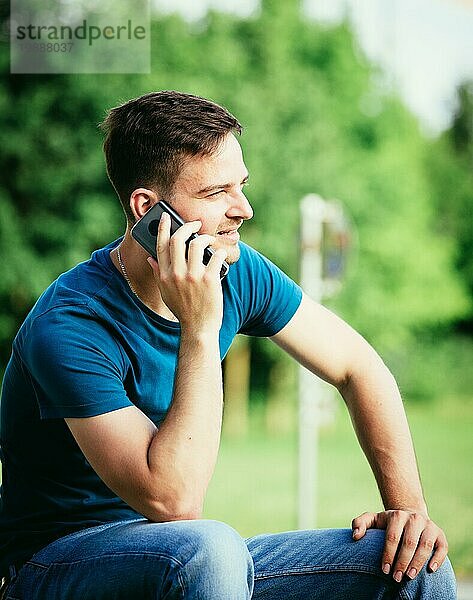 Hübscher junger Mann sitzt im Freien und spricht mit jemandem am Telefon