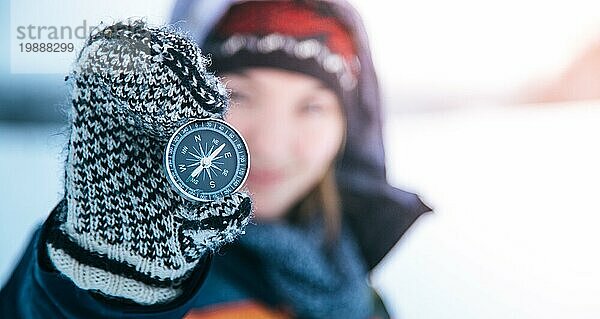 Junge lächelnde Frau hält einen Kompass hoch. Winterzeit  Handschuhe und Kapuze