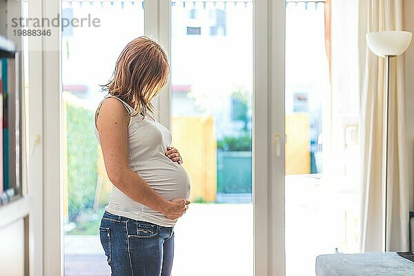 Glückliche kaukasische schwangere Mutter  die ihren Bauch berührt  Blue Jeans  Nahaufnahme