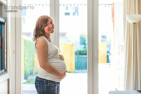 Glückliche kaukasische schwangere Mutter  die ihren Bauch berührt  Blue Jeans  Nahaufnahme