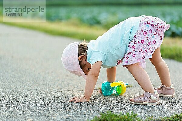 Baby sitzt auf einer asphaltierten Straße zwischen ländlichen landwirtschaftlichen Feldern. Kinder im Freien Konzept