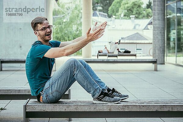 Männlicher junger Angestellter sitzt im Freien und macht eine Geste. Städtische Geschäftsumgebung