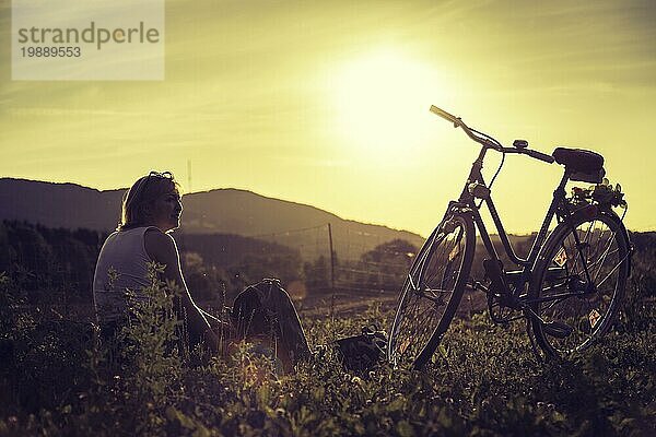 Junge Frau mit Fahrrad genießt die Abendsonne