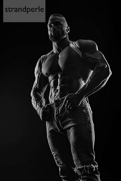 Silhouette eines starken Bodybuilders. Selbstbewusster junger Fitness Sportler mit einem kräftigen Körper und perfekten Bauchmuskeln. Schwarz Weiß Fotografie. Dramatisches Licht. Gemischte Medien