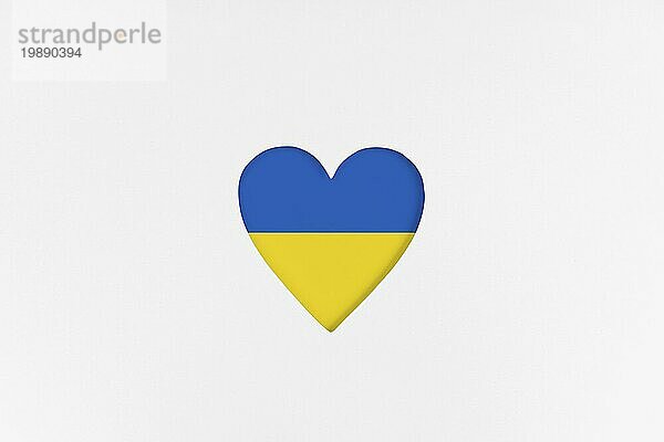 Ukraine Flagge auf Herzform vor weißem Hintergrundem Karton Hintergrund. Bedruckter Karton mit ausgestanzter Herzform. Ansicht von oben