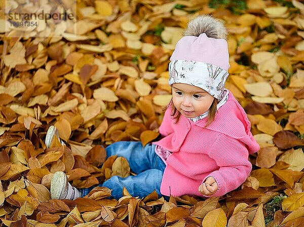 Baby Mädchen im Herbst Park sitzen in Haufen von trockenen Blättern Spaß haben. Eggenberg Park in Graz Österreich