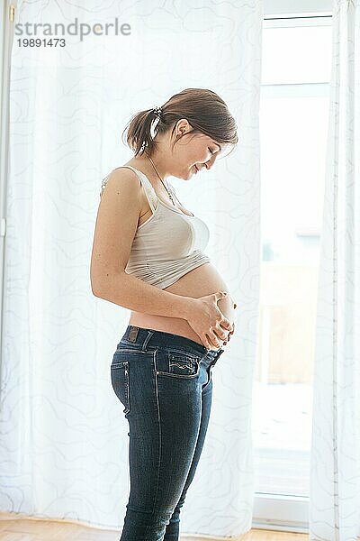 Glückliche kaukasische schwangere Mutter  die ihren nackten Bauch berührt  Blue Jeans  Nahaufnahme