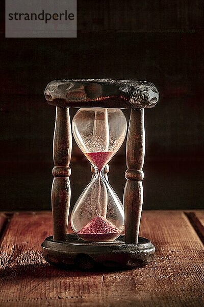 Die Zeit läuft aus Konzept. Ein Stundenglas mit Sand fallen durch  auf einem dunklen rustikalen Hintergrund