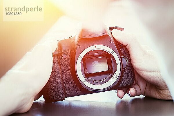 Die Hände des Fotografen berühren eine professionelle Spiegelreflexkamera mit offenem Sensor. Sonnenlicht