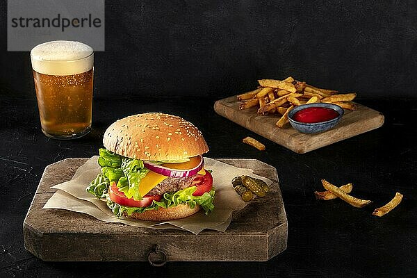 Burger mit Pommes frites und Bier. Hamburger mit Rindfleisch  Käse  Zwiebel  Tomate und grünem Salat  auf dunklem Hintergrund mit Platz für Text. Selektiver Fokus