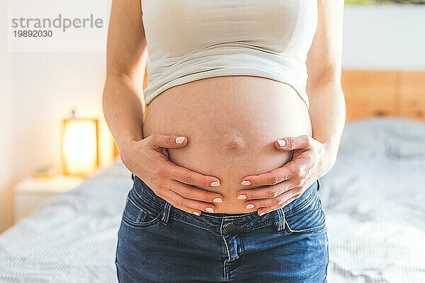 Kaukasische schwangere Mutter  die ihren nackten Bauch berührt  Blue Jeans  Nahaufnahme