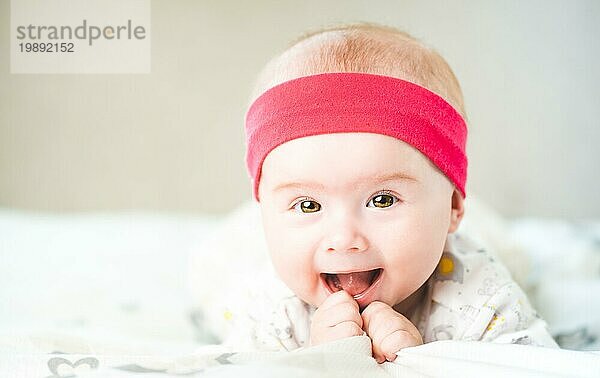 Adorable Baby Mädchen mit roten Stirnband Blick in Richtung Kamera und lächelnd. Gesundheit Konzept. 6 Monate altes Baby. Raum kopieren