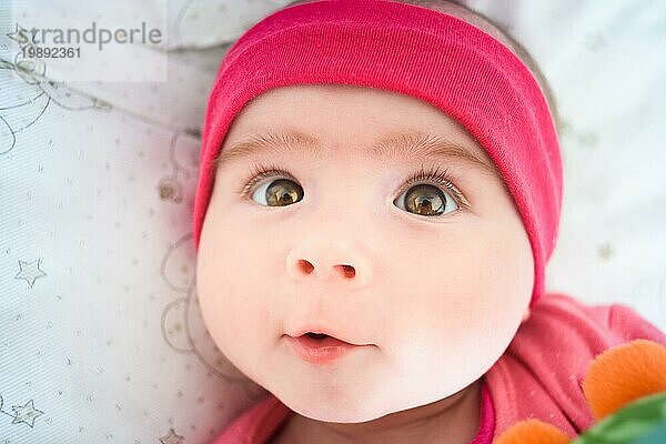 Schönes Porträt von 5 Wochen alten Baby Mädchen in einer Krippe liegt und schaut nach oben in Richtung Kamera. Baby Pflege Konzept