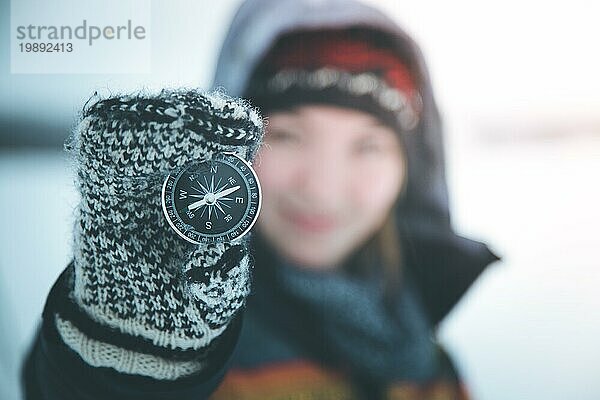 Junge lächelnde Frau hält einen Kompass hoch. Winterzeit  Handschuhe und Kapuze