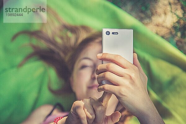 Schönes Mädchen benutzt ihr Smartphone auf einer Decke im Park liegend  Ansicht von oben