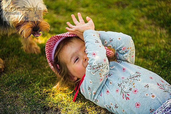 Baby Mädchen liegt auf Gras mit Hund im Hinterhof am Sommertag. Haustier mit Kindern Konzept