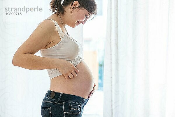 Glückliche kaukasische schwangere Mutter  die ihren Bauch berührt  Blue Jeans  Nahaufnahme