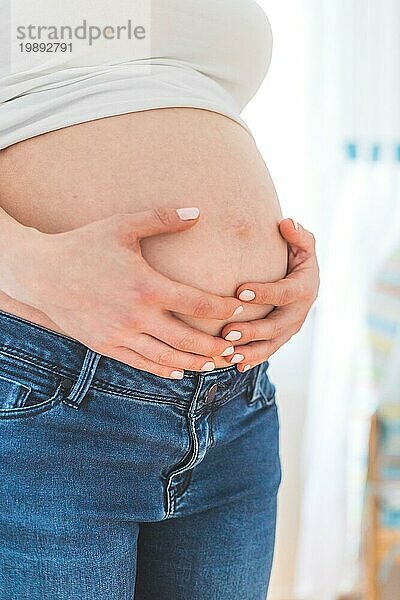 Kaukasische schwangere Mutter  die ihren nackten Bauch berührt  Blue Jeans  Nahaufnahme