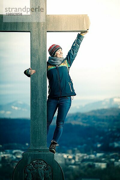 Junges Mädchen steht stolz und glücklich auf einem Gipfelkreuz  Herbst