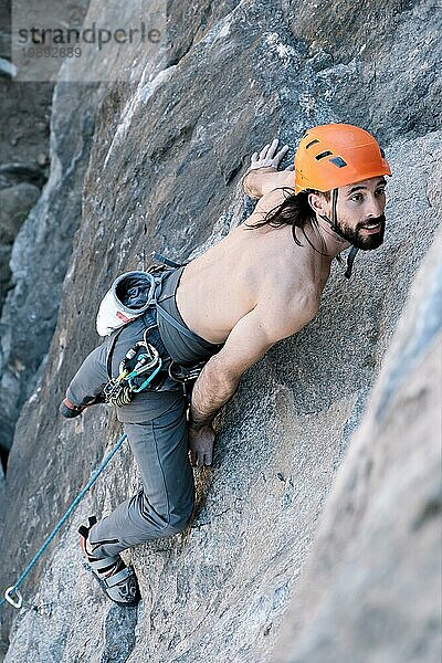Person beim Klettern im Hochgebirge mit Seil ohne Hemd und orangefarbenem Helm in der Wildnis. Konzept von Vertrauen und Risiko  Sicherheit und Selbstverbesserung