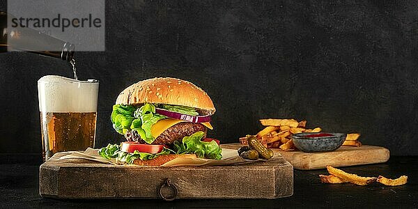 Burger und Bier Panorama. Hamburger mit Rindfleisch  Käse  Zwiebel  Tomate und grünem Salat  eine Seitenansicht auf einem dunklen Hintergrund mit einem Platz für Text. Selektiver Fokus