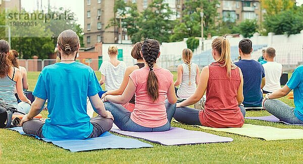 Yogagruppe junger Mädchen und Männer meditiert im Park sitzend