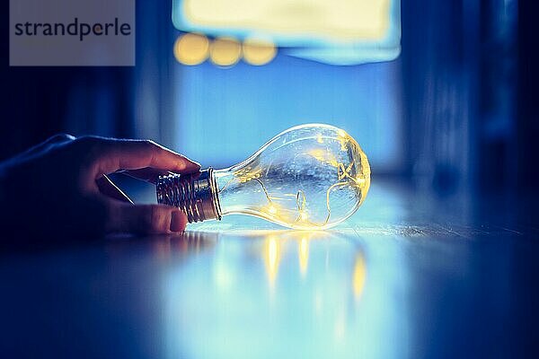 Die Hände halten eine LEDglühbirne über dem Holzboden. Symbol für Ideen und Innovation. Fenster und Licht im unscharfen Hintergrund