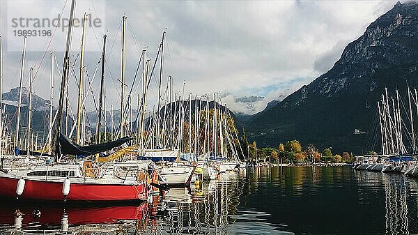 Anlegen von Segelyachten auf einem Bergsee gegen Bergsilhouetten und Wolken  Blick auf den Yachthafen mit bunten Segelbooten  Herbstlandschaft